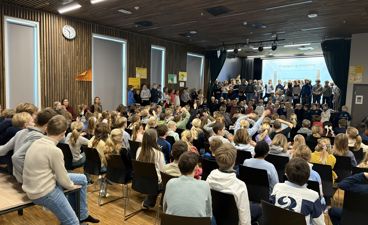 en gruppe mennesker som sitter i et rom med en stor skjerm