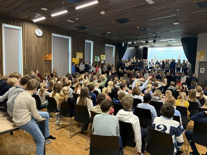 en gruppe mennesker som sitter i et rom med en stor skjerm