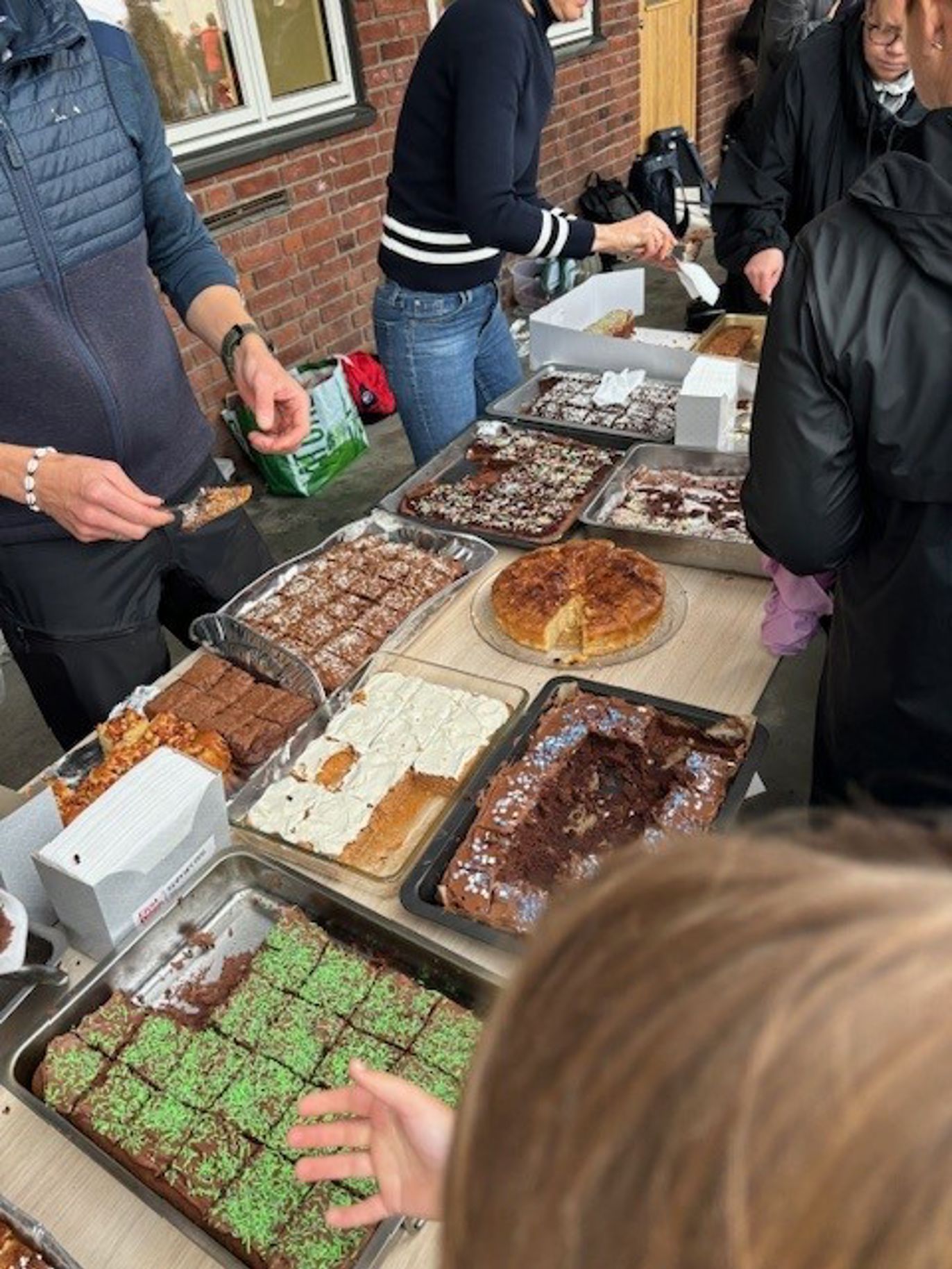 En gruppe mennesker står rundt et bord fullt av bakverk